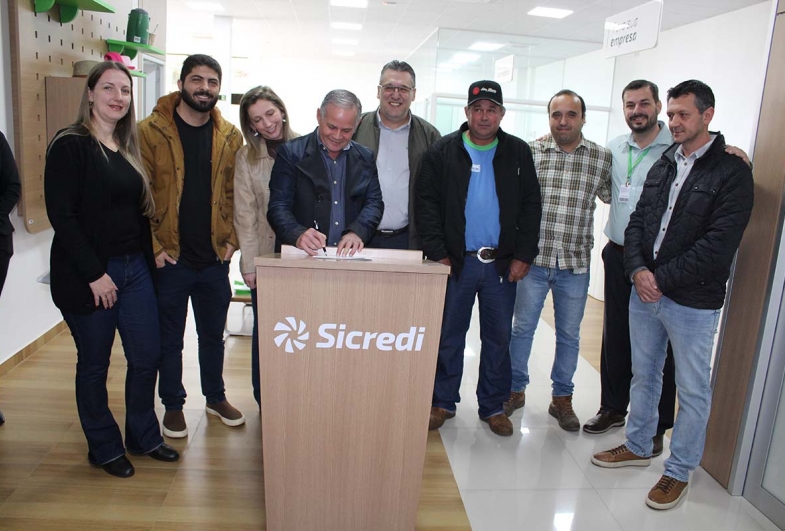 Prefeito Edinho assina documento da parceria com o Sicredi ladeado pela presidente da Câmara Regina, presidente da festa  Fernando, primeira-dama Pety, diretor executivo do Sicredi Neuri Saggin, Adria